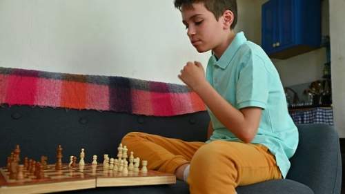 Adolescente sentado em uma mesa jogando xadrez, concentrado na próxima jogada.