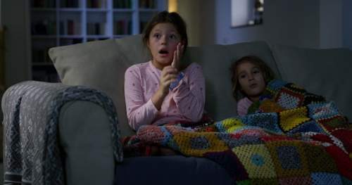 Duas crianças sentadas no sofá assistindo a um filme durante as férias.