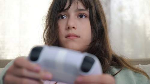 Menina segurando um controle enquanto joga videogame em casa.