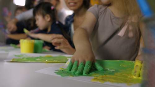 Meninas com as mãos pintadas de cores vibrantes criando uma arte com pintura à mão.