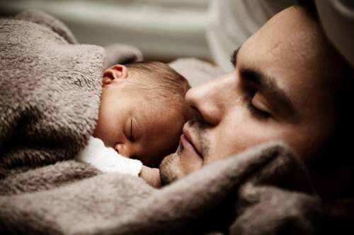 Por que a paternidade ativa é essencial para a formação dos filhos? Pai e filho dormindo juntos, com o pai segurando o filho no colo.